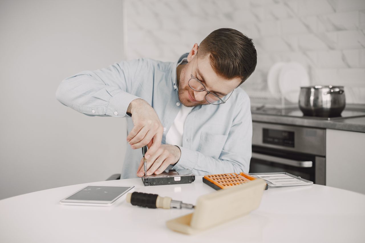 Man wearing glasses using a screwdriver to fix a device on a kitchen table.
